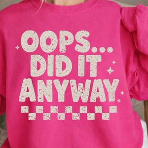 Puede incluir: Una sudadera rosa brillante con el texto "OOPS... DID IT ANYWAY" en una fuente blanca desgastada. La sudadera tiene cuello redondo y mangas largas.