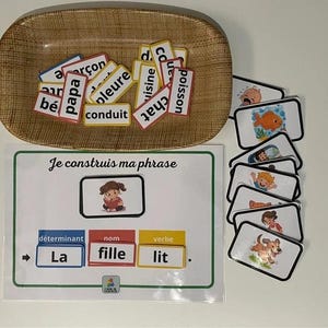 Könnte beinhalten: Lernspiel mit Wortkarten und Illustrationen. Ein rechteckiges Holztablett enthält Wortkarten mit französischen Wörtern. Eine Karte lautet "Je construis ma phrase" mit einer Satzstrukturführung. Zusätzliche Karten zeigen Illustrationen.