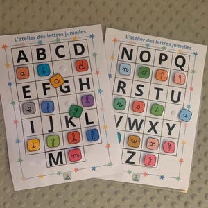 Peut inclure: Deux cartes éducatives pour apprendre l'alphabet avec le texte "L'atelier des lettres jumelles". Chaque carte présente une grille avec des lettres majuscules et minuscules, et des tuiles de lettres colorées. Les cartes sont conçues à des fins éducatives.