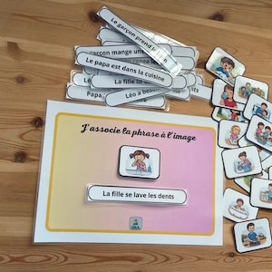 Può includere: Gioco educativo con carte illustrate ed etichette di testo. Il gioco include un foglio con il testo "J'associe la phrase à l'image" e la frase "La fille se lave les dents". Carte ed etichette aggiuntive su una superficie di legno.