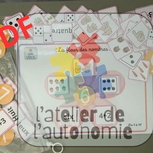 May include: A set of educational learning cards and a central mat titled La fleur des nombres, featuring numbers, hand signs, dice patterns, and addition problems. The cards are white with red borders, and some are circular orange tokens with numbers.