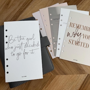 May include: A gray leather planner with several planner inserts. One insert reads "Be the girl who just decided to go for it." Another insert reads "Remember why you started."