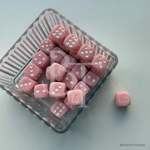 May include: A collection of pink dice with white Hello Kitty faces, in a clear glass container with a ribbed design.