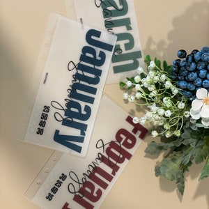 May include: Three clear plastic sheets with the months of February, January, and March printed in bold, dark lettering. The text is in a cursive font. The sheets are designed for a planner or journal.