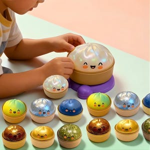 Puede incluir: Una colección de juguetes de bolas de masa hervida sonrientes y coloridos. Los juguetes tienen una parte superior nacarada, iridiscente o de color sólido y una base beige. Los juguetes están dispuestos sobre una superficie verde claro. Las manos de un niño interactúan con los juguetes.