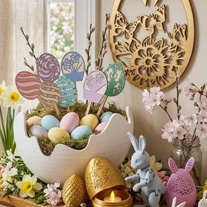 May include: Easter-themed decor featuring a white egg-shaped bowl filled with pastel-colored eggs and decorative egg-shaped cutouts on sticks. A gold egg-shaped candle holder, bunny figurines, and a wooden egg-shaped wall hanging with butterfly cutouts complete the display.