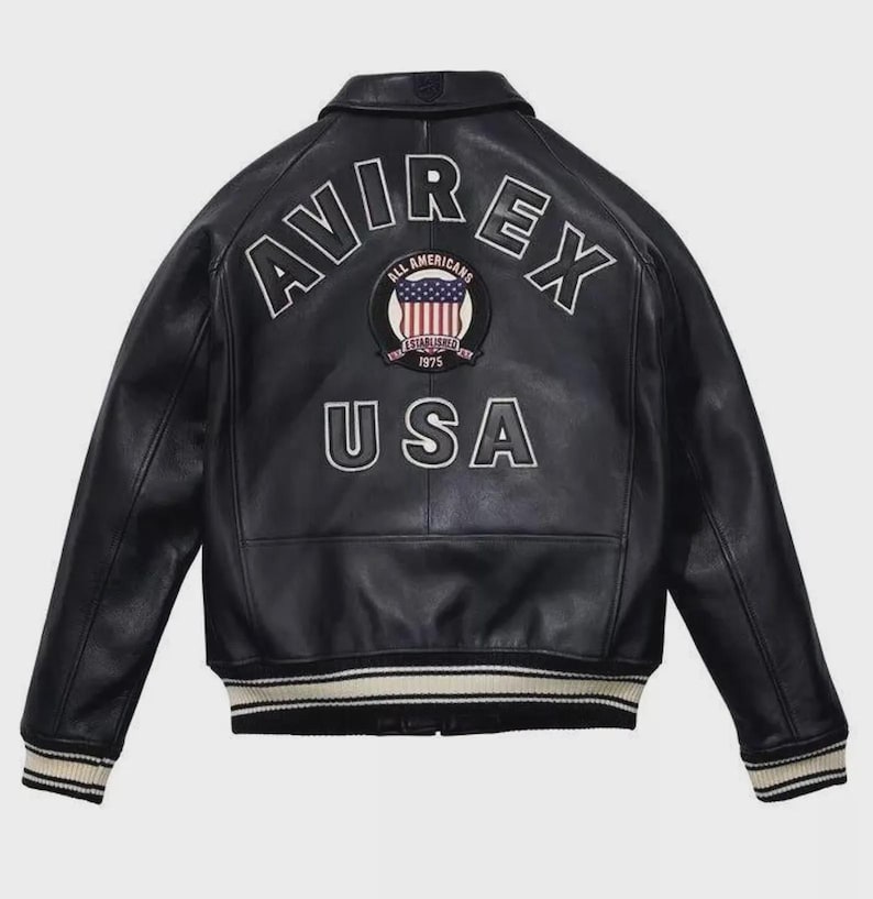 May include: Black leather jacket with the text "AVIREX" and "USA" on the back. The jacket features a patch with the American flag and the words "ALL AMERICANS ESTABLISHED 1975". The jacket has a ribbed collar, cuffs, and hem.