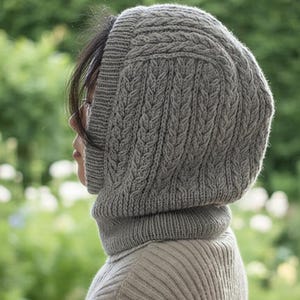 May include: A gray knitted hood with a cable knit design and a ribbed neck warmer. The hood covers the head and neck, providing warmth and protection. The knitted hood is a cozy accessory for cold weather.