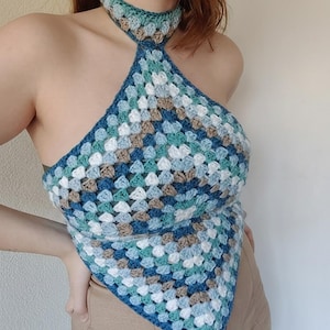 May include: A handmade crochet halter top in a granny square pattern. The top features a colour palette of blues, white, and brown. The halter neck and triangle shape create a unique and stylish design. This top is a fashionable addition to any wardrobe.