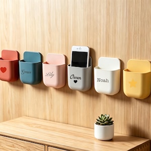 Peut inclure: Six poches de rangement murales en rouge, bleu, rose, gris, blanc et jaune. La poche rouge a un cœur, la bleue indique Grace, la rose Lily, la grise contient un smartphone et indique Owen avec un cœur, la blanche Noah et la jaune une étoile.
