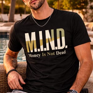 May include: Black crew neck t-shirt with the text "M.I.N.D. Money Is Not Dead" in white and olive green. The person is wearing sunglasses, a silver chain, a watch, and a bracelet. The person is sitting outside.