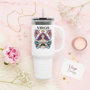 May include: White travel mug with a handle and a silver lid, featuring a colorful Virgo design. The design includes a woman with purple hair, flowers, and the word "Virgo". A gold necklace and earrings are also visible.