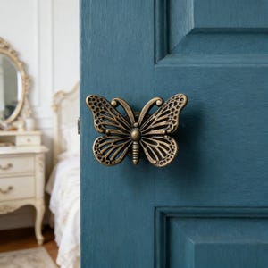 May include: A bronze butterfly door knob is fixed to a teal blue door. The butterfly design features intricate wing patterns and a central body. The door knob provides a decorative element to the door.