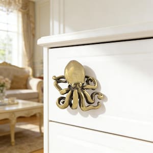 May include: A bronze-colored octopus-shaped cabinet pull mounted on a white cabinet drawer. The octopus has detailed tentacles and a textured surface. The cabinet is part of a larger furniture set.