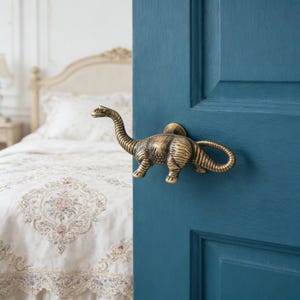 May include: A brass dinosaur-shaped door handle is mounted on a teal blue door. The dinosaur has a long neck and tail, with detailed texture. The handle adds a whimsical touch to the door's design.
