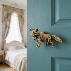 Könnte beinhalten: Ein bronzefarbener Türgriff in Form eines Fuchses, montiert an einer türkisfarbenen Tür. Der Fuchs steht aufrecht und hat eine detaillierte Fellstruktur. Im Hintergrund ist ein Schlafzimmer mit Bett und Vorhängen zu sehen.