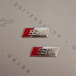Könnte beinhalten: Zwei silberne und rote S-Line-Autoembleme. Die Embleme haben eine rechteckige Form mit rotem Hintergrund auf der linken Seite und dem Text "S line" in Silber.