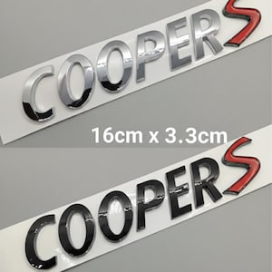 May include: Two car emblem sets. One set is silver, the other is black. Both sets read "COOPERS" with a red "S" and are 16cm x 3.3cm. The text is on a white background.