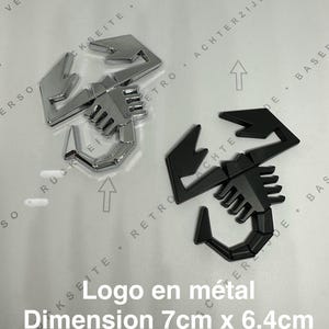Könnte beinhalten: Zwei Metall-Skorpion-Logos, eines silberfarben und eines schwarz, werden gezeigt. Das silberne Logo ist stark reflektierend. Der Text "Logo en métal" und "Dimension 7cm x 6.4cm" ist sichtbar. Die Logos messen 7 cm x 6,4 cm.