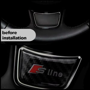 May include: Black car steering wheel with a carbon fibre S line emblem. The image shows the steering wheel before installation. The S line logo is red and the text is silver.