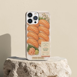 May include: A phone case featuring a graphic print of salmon nigiri sushi arranged in a plastic-wrapped tray. The design includes a label with the text SOLAKA MARKET, FRESH PICKS, JAPANESE SALMON NIGIRI, and a barcode at the bottom edge.