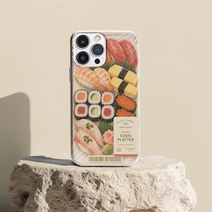 May include: A smartphone case featuring a graphic print of a plastic-wrapped sushi platter with tuna, shrimp, egg, cucumber rolls, and salmon roe. A label reads SOLANA MARKET FRESH PICKS JAPANESE SUSHI PLATTER. A barcode is printed at the bottom edge.