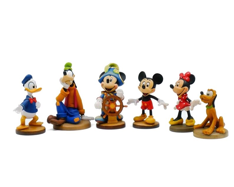 May include: A collection of Disney character figurines, including Donald Duck, Goofy, Mickey Mouse, Minnie Mouse, and Pluto. Each figurine is brightly colored and stands on a small, round base. The characters are in various poses.