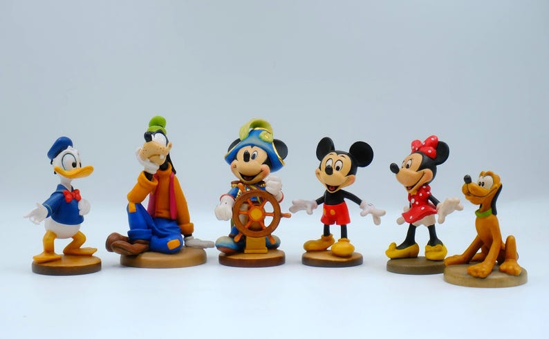 May include: A collection of Disney character figurines, including Donald Duck, Goofy, Mickey Mouse, Minnie Mouse, and Pluto. The figures are brightly colored and stand on individual bases, showcasing classic cartoon designs.