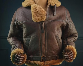 May include: A brown leather bomber jacket with a shearling collar and cuffs. The jacket features a front zipper, a waist belt, and two front pockets. The jacket is displayed on a mannequin.