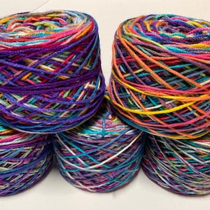 May include: Five skeins of multi-coloured yarn, tightly wound into balls. The yarn features shades of purple, pink, blue, orange, and yellow. Ideal for knitting or crochet projects, the yarn is presented in a neat stack.