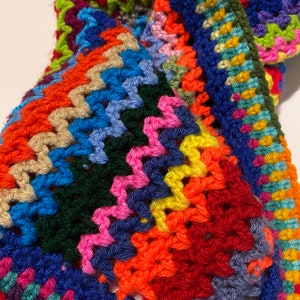 May include: A colorful crocheted blanket with a multi-colored border. The blanket is made with a variety of different colored yarns, including red, orange, yellow, green, blue, purple, and pink.