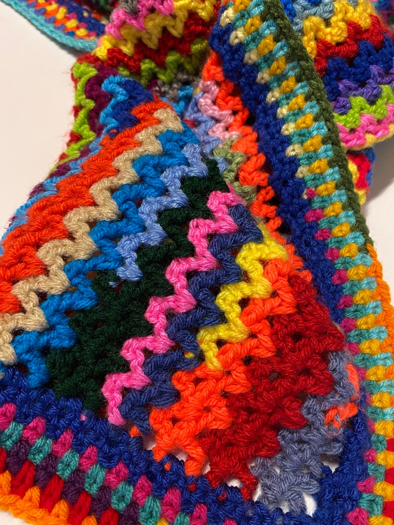 May include: A colorful crocheted blanket with a multi-colored border. The blanket is made with a variety of different colored yarns, including red, orange, yellow, green, blue, purple, and pink.