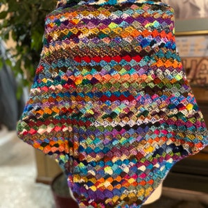 May include: A colorful crocheted shawl with a variety of colors, including blue, green, purple, and red. The shawl is made with a granny square stitch and has a triangular shape.