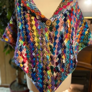 May include: A colorful crocheted shawl with a wooden button closure. The shawl is made with a variety of different colored yarns, creating a unique and eye-catching design.