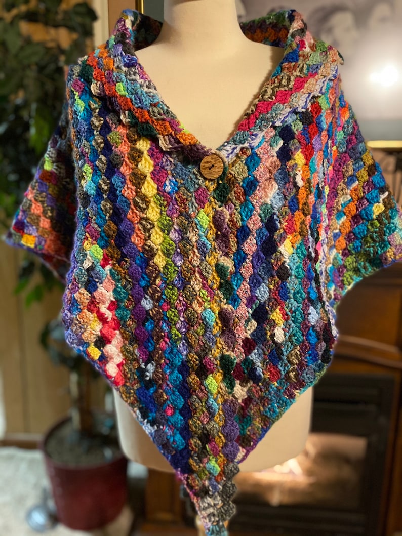 May include: A colorful crocheted shawl with a wooden button closure. The shawl is made with a variety of different colored yarns, creating a unique and eye-catching design.