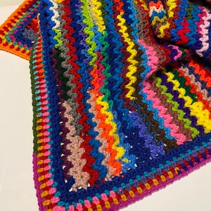 May include: A colorful crocheted blanket with a multi-colored striped pattern and a contrasting border. The blanket is made with a variety of yarn colors, including red, orange, yellow, green, blue, purple, and pink.