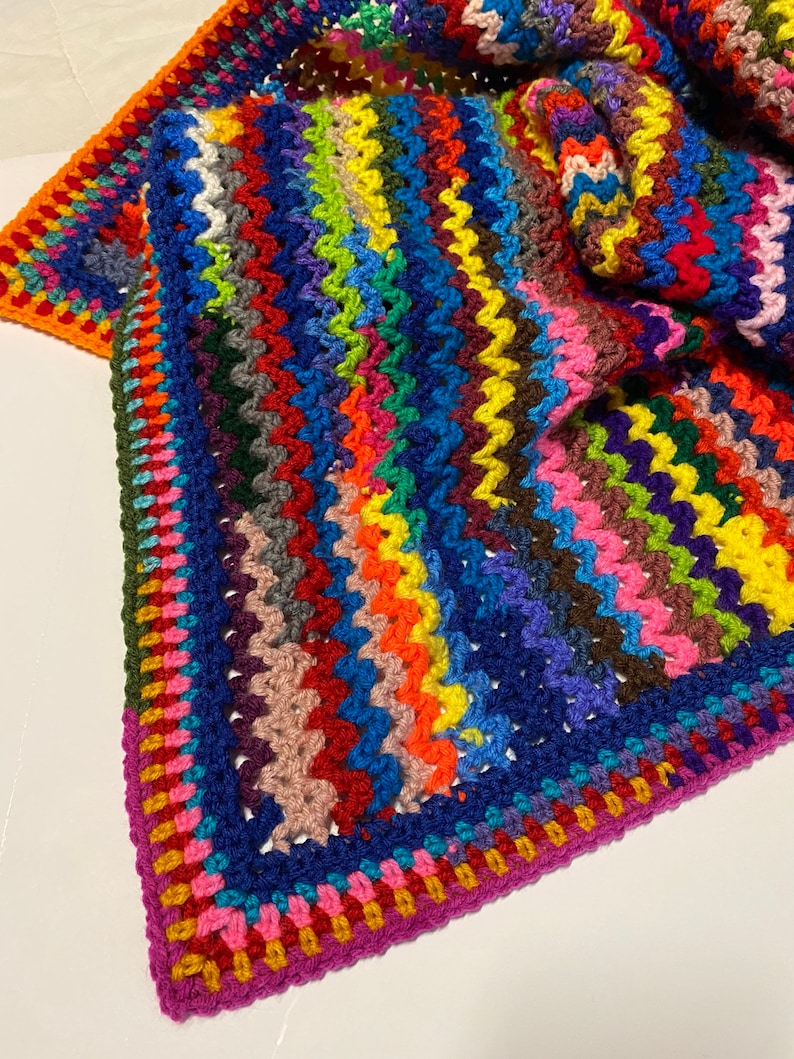 May include: A colorful crocheted blanket with a multi-colored striped pattern and a contrasting border. The blanket is made with a variety of yarn colors, including red, orange, yellow, green, blue, purple, and pink.
