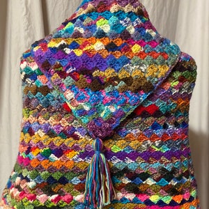 May include: A multi-colored crocheted shawl with a tassel. The shawl is made with a variety of different colored yarns and has a scalloped edge.