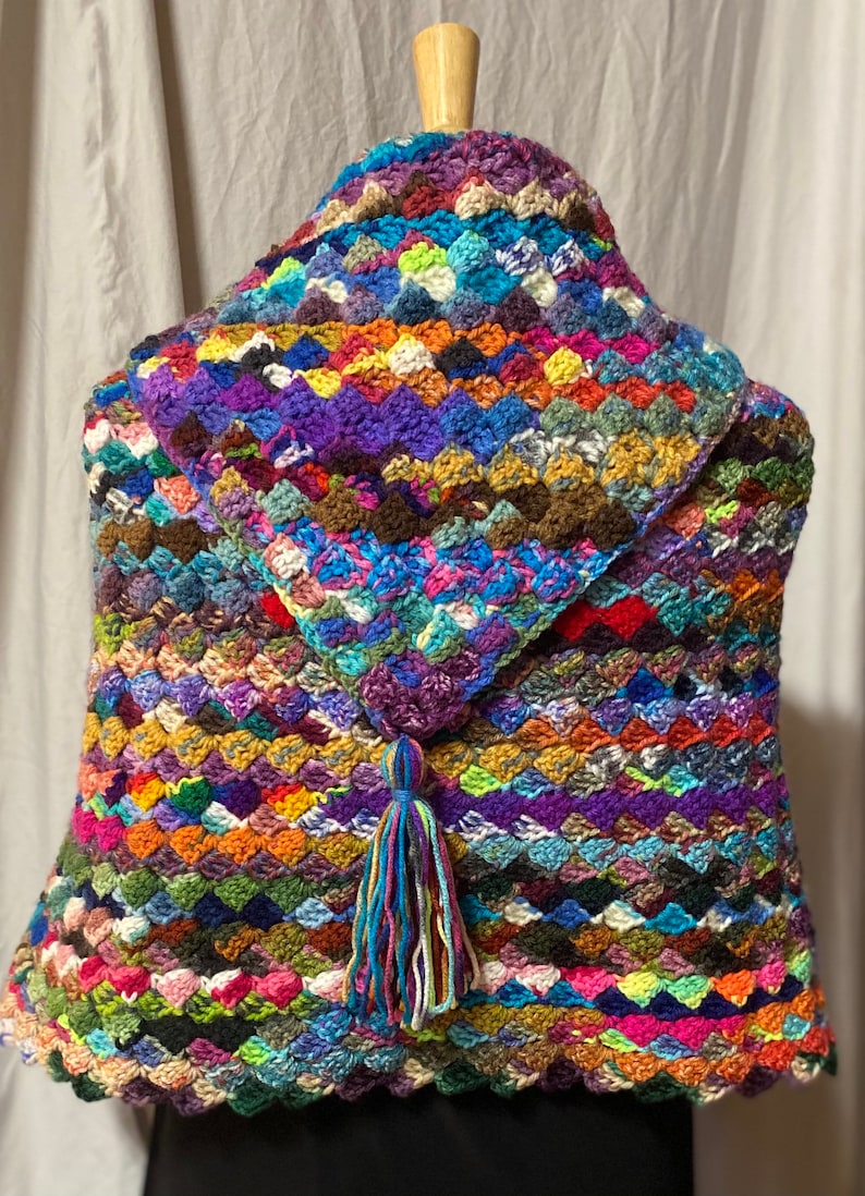 May include: A multi-colored crocheted shawl with a tassel. The shawl is made with a variety of different colored yarns and has a scalloped edge.