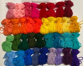May include: A rainbow assortment of yarn skeins in various colors, including pink, red, orange, yellow, green, blue, purple, and dark purple. The yarn is arranged in rows, with each row containing a different color.