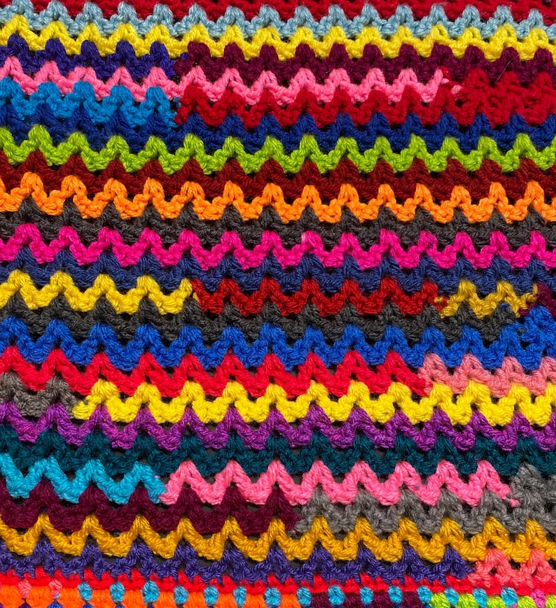 May include: A colorful crocheted blanket with a wavy pattern. The blanket is made with a variety of bright colors, including red, orange, yellow, green, blue, purple, and pink.