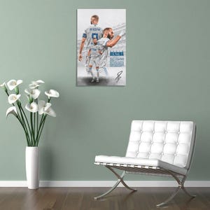 Może przedstawiać: Oprawiony wydruk przedstawiający piłkarza w białej koszulce z niebieskimi akcentami. Wydruk zawiera wiele zdjęć zawodnika, imię "BENZEMA" i podpis. Tło sugeruje stadion.