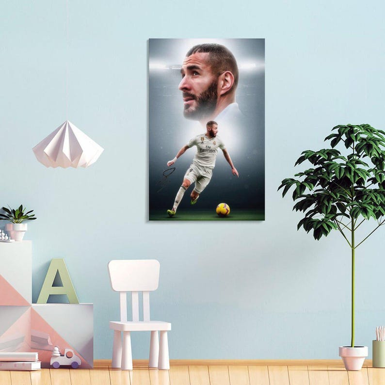 以下が含まれることがあります： 白いユニフォームを着て、緑のフィールドで黄色のサッカーボールを蹴るサッカー選手が描かれた額入りのプリント。選手の頭上には、選手の顔の肖像画があります。背景は明るい照明のあるスタジアムです。