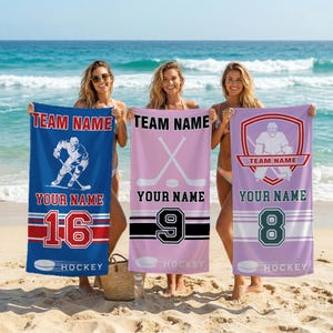 Könnte beinhalten: Drei Strandtücher mit Hockey-Motiven. Eines ist blau mit einer Hockey-Spieler-Grafik, ein anderes ist rosa mit gekreuzten Hockeyschlägern und das dritte ist lavendelfarben mit einer Hockey-Spieler-Silhouette. Jedes Handtuch hat Platz für einen Teamnamen, einen Namen und eine Nummer.