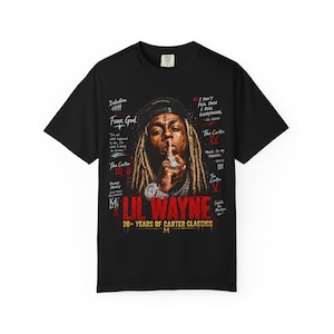 Puede incluir: Una camiseta negra con un gr&aacute;fico de Lil Wayne con rastas, gorra y joyas. El dise&ntilde;o incluye texto como "LIL WAYNE", "20+ YEARS OF CARTER CLASSICS", "Fear God", "Tha Carter III", "Tha Carter IV", "Tha Carter V" y varias citas impresas.