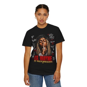Puede incluir: Una camiseta negra de manga corta con un gr&aacute;fico de Lil Wayne con rastas, gorra y joyas. El dise&ntilde;o incluye texto en rojo que dice LIL WAYNE, 20+ YEARS OF CARTER CLASSICS, y varias citas y t&iacute;tulos de &aacute;lbumes en color blanco.