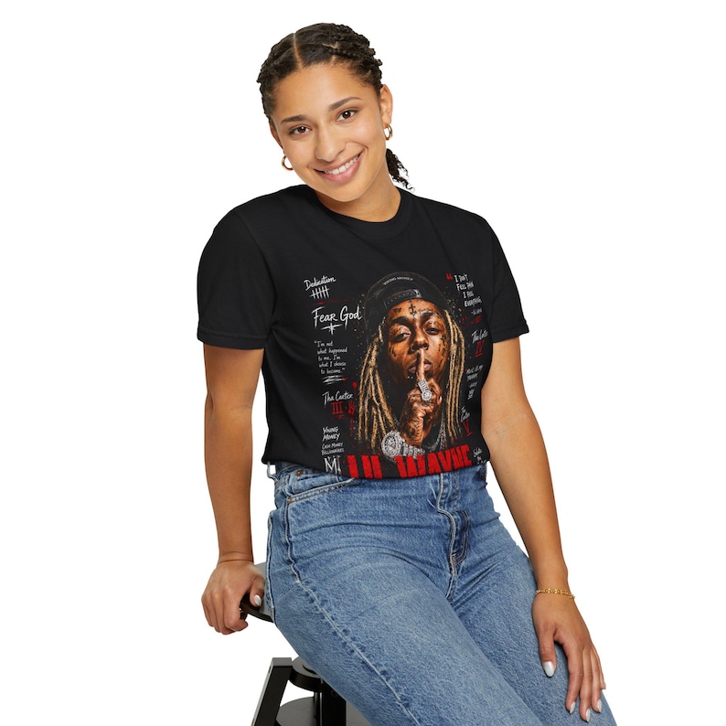 Puede incluir: Una camiseta negra de manga corta con un estampado gr&aacute;fico de Lil Wayne con rastas, gorra y joyas. El dise&ntilde;o incluye elementos de texto en rojo y blanco como Fear God, The Carter y Young Money, con un retrato centrado en la prenda.