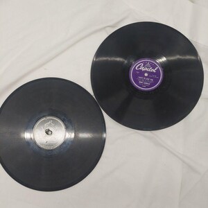 May include: Two circular black vinyl records. One record features a purple Capitol label with the text I Hate To Lose You, Benny Goodman and His Orchestra. The other record has a silver Victor label with a small dog logo and text.