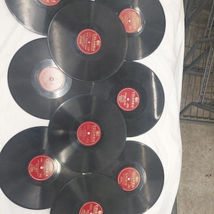 May include: A collection of eight black circular vinyl records arranged in a cluster. Each record features a prominent red center label with the word Columbia printed in white text, along with additional black printed details on the labels.