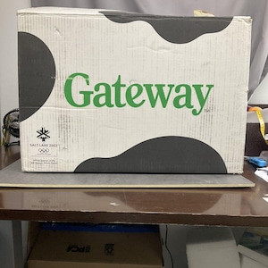 May include: A rectangular cardboard box with a white background and black cow-print spots. The word Gateway is printed in large green letters. Below the text, a Salt Lake 2002 Olympic Winter Games logo is visible with the text Official Sponsor.